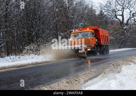 Ein großes Auto mit einem Pflug befreit die Straße von Schnee. Die Sonderausrüstung Orange Cargo kämpft im Winter mit den Elementen. Beseitigung der Auswirkungen von t Stockfoto