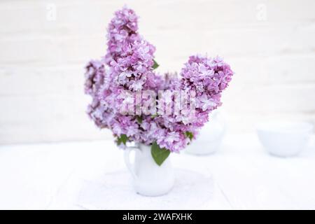 Ein Haufen lila Fliederblüten auf weißem Tisch in Vase, Inneneinrichtung mit Details. Blumenstrauß im Frühling zu Hause. Stockfoto