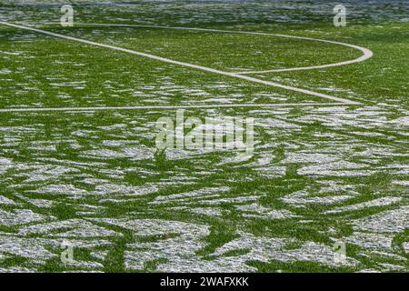 Das Fußballfeld mit Kunstrasen ist mit einer leichten Schneeschicht bedeckt. Frühling. Grünes Gras auf dem Fußballfeld ist von zu sehen Stockfoto