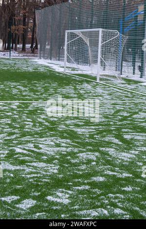 Fußballfeld im Winter, künstliches Gras auf freiem Schnee im Ferntor und Netz. Stockfoto
