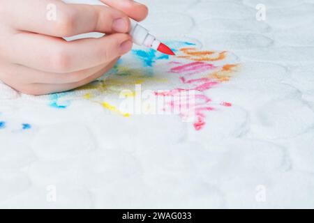 Ein Kind zeichnet Filzstifte auf die weißen Polstermöbel des Sofas oder Teppichs. Draufsicht. Stockfoto