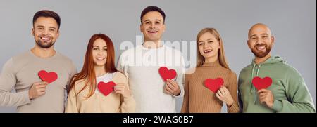 Junge und lächelnde Freiwillige mit roten Herzen auf grauem Hintergrund Stockfoto