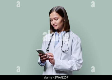 Junge Ärztin mit Smartphone, auf grünem Atelierhintergrund Stockfoto