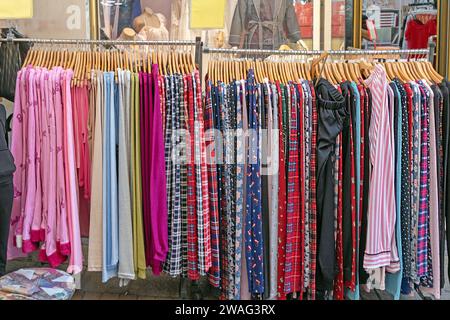 Bunte Kleidung hängt an Regalen und wird draußen auf einem Markt verkauft Stockfoto
