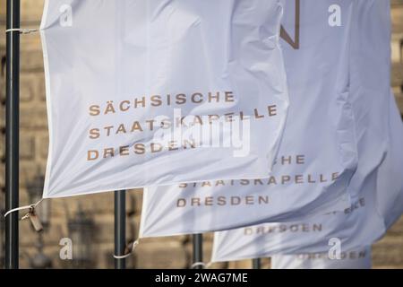 Dresden, Deutschland. Januar 2024. Fahnen mit der Aufschrift „Sächsische Staatskapelle Dresden“ winken im Wind vor der Semperoper. Robert Michael/dpa/Alamy Live News Stockfoto