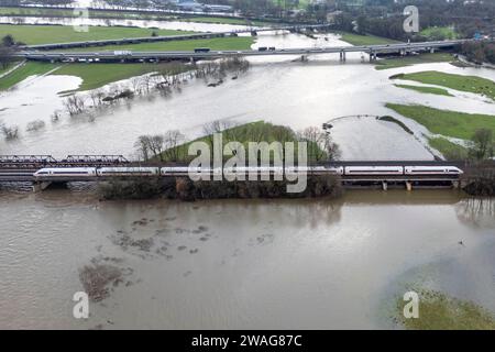 04. Januar 2024, Nordrhein-Westfalen, Mülheim an der Ruhr: Ein EISZUG überquert eine Brücke in den von Hochwasser überfluteten Ruhrwiesen. (Luftaufnahme mit Drohne) Foto: Christoph Reichwein/dpa Stockfoto
