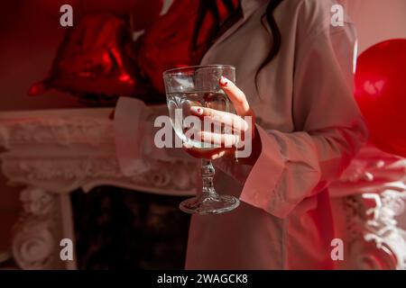 Nahaufnahme der Frauenhand mit Glas Champagner mit festlicher Maniküre mit roten Herzen auf dem Nagel, Silberring. Valentinstag Feiern, Engagement Stockfoto