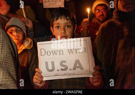 Srinagar, Indien, 01.04.2024, Ein schiitisches Kind aus Kaschmir hält während einer Mahnwache bei Kerzenschein ein Plakat mit der Aufschrift „unten mit den USA“. Am Rande von Srinagar, Kaschmir, hielten schiitische Muslime aus der kaschmirischen Gemeinde eine Mahnwache bei Kerzenlicht ab, in der sie ihren Widerstand gegen Israel und die Vereinigten Staaten zum Ausdruck brachten. Die feierliche Versammlung nahm eine tragische Wende, als 84 Personen ihr Leben verloren und zahlreiche andere während einer Zeremonie zum Gedenken an den Tod des iranischen Generals Qassem Soleimani in einer Explosion verletzt wurden. Der Islamische Staat übernahm die Verantwortung für die beiden zerstörerischen Explosionen, die zu den Toten führten Stockfoto