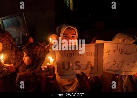 Schiitische Kinder aus Kaschmir halten während einer Mahnwache Kerzen und ein Plakat „Shame on USA“. Am Rande von Srinagar, Kaschmir, hielten schiitische Muslime aus der kaschmirischen Gemeinde eine Mahnwache bei Kerzenlicht ab, in der sie ihren Widerstand gegen Israel und die Vereinigten Staaten zum Ausdruck brachten. Die feierliche Versammlung nahm eine tragische Wende, als 84 Personen ihr Leben verloren und zahlreiche andere während einer Zeremonie zum Gedenken an den Tod des iranischen Generals Qassem Soleimani in einer Explosion verletzt wurden. Der Islamische Staat übernahm die Verantwortung für die beiden zerstörerischen Explosionen, die am Vorabend zum Tod von 84 Menschen führten Stockfoto