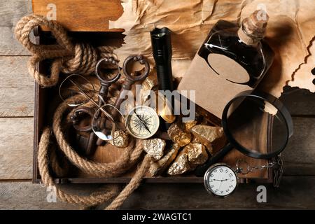 Box mit Reiseausrüstung, goldenen Nuggets und Flasche Rum auf braunem Holzhintergrund Stockfoto