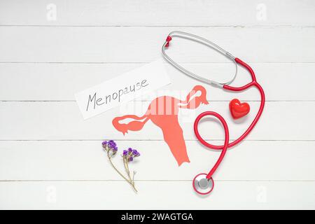 Wort-MENOPAUSE mit Papier Uterus, Blumen und Stethoskop auf weißem hölzernem Hintergrund Stockfoto
