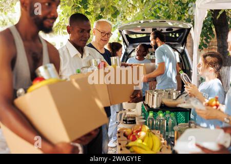 Gruppe von Einzelpersonen lächelt, während sie Essensboxen und Konserven an Bedürftige verteilt. Junge Freiwillige leisten gerne humanitäre Hilfe für obdachlose Senioren und Menschen, die Zuflucht suchen. Stockfoto