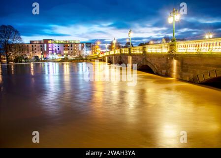 Bei Sonnenuntergang, nach stürmischem, nassem Wetter, beträchtliche Regenwasserbäche, die unter der beleuchteten historischen Brücke, entlang der Severn, nach dem Eingießen passieren Stockfoto