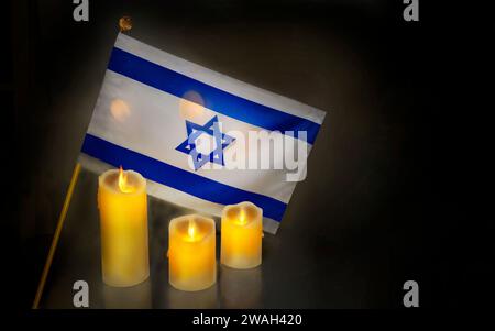 Brennende Kerzen mit Flagge Israels vor dunklem Hintergrund mit Platz für Text. Internationaler Holocaust-Gedenktag. Stockfoto
