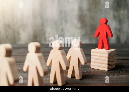 Rote Holzfiguren heben sich von der Menge der Holzfiguren ab. Führungskonzept Stockfoto