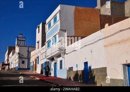 Zurück von einer Einheimischen, die einen schwarzen Chador trägt, die auf dem fotogenen Boulevard Moulay Youssef in Sidi Ifni, Marokko, läuft. Stockfoto