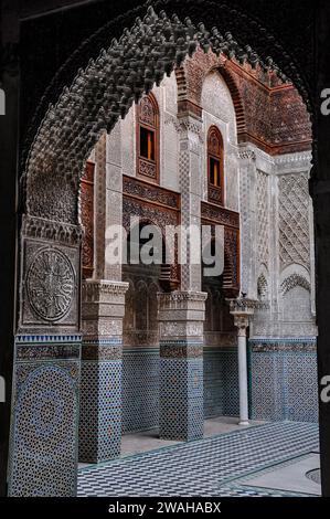 Al-Attarine Madrasa, eine religiöse Schule aus dem 14. Jahrhundert in Fes, Marokko. Blick auf den Innenhof unter einem Bogen mit kompliziertem maurischem Stuck Stockfoto