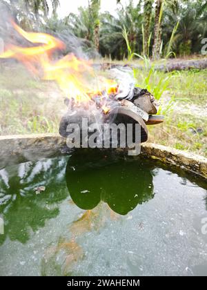 Alte, weggeworfene Schuhe auf Flamme am Rand des zylindrischen Betonbrunnens. Stockfoto