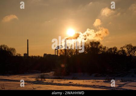 Rauchschornsteine eines Heizraumes vor der Kulisse einer hellen untergehenden Sonne im Winter Stockfoto