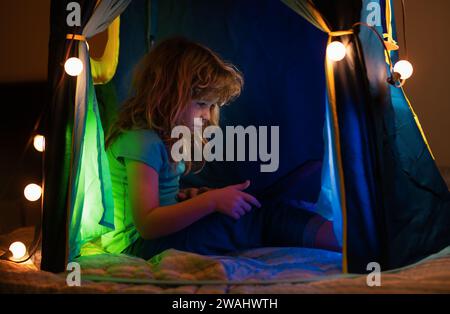Kind liegt im Bett und lernt in der virtuellen Online-Schulklasse. Kind, das zu Hause am Laptop-Internet arbeitet. Kind, das einen Laptop verwendet. Homeschooling für Stockfoto