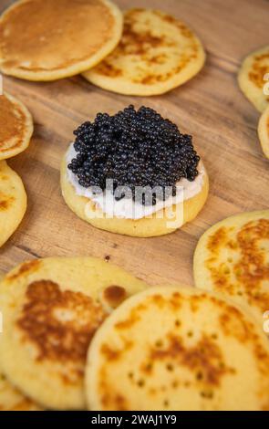 Blinis mit schwarzem Kaviar und Frischkäse, auf festlichem Gericht, Mini-Pfannkuchen, eine elegante Vorspeise Stockfoto