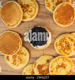 Blinis mit schwarzem Kaviar und Frischkäse, auf festlichem Gericht, Mini-Pfannkuchen, eine elegante Vorspeise Stockfoto