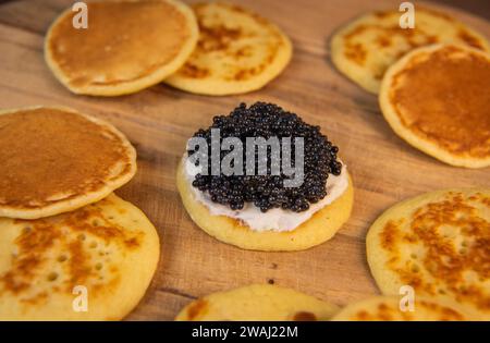 Blinis mit schwarzem Kaviar und Frischkäse, auf festlichem Gericht, Mini-Pfannkuchen, eine elegante Vorspeise Stockfoto