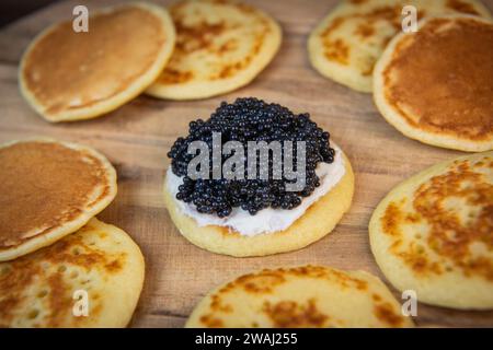 Blinis mit schwarzem Kaviar und Frischkäse, auf festlichem Gericht, Mini-Pfannkuchen, eine elegante Vorspeise Stockfoto