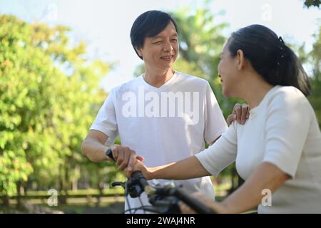 Glückliches Paar mittleren Alters, das an einem schönen sonnigen Tag im Park Fahrrad fährt, lacht und Spaß hat. Stockfoto