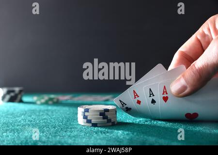 Hand zeigt vier Asse, die Karten auf einem Tisch mit grüner Matte mit dunklem isoliertem Hintergrund spielen. Vorderansicht. Stockfoto