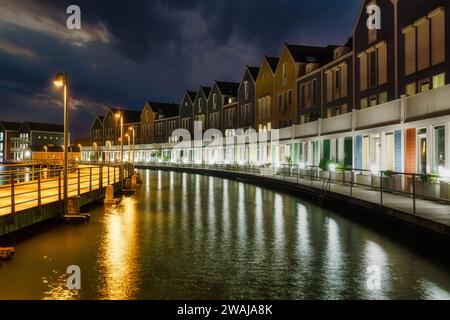 Nächtlicher Blick auf beleuchtete Reihenhäuser entlang eines Kanals in Houten, Niederlande, die sich auf dem Wasser spiegeln Stockfoto