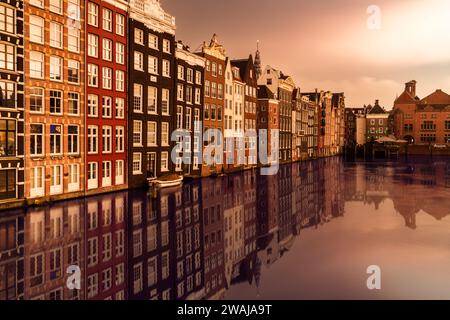 Golden Hour Reflexionen auf dem Wasser mit einer Reihe farbenfroher traditioneller niederländischer Häuser entlang des Kanals in Amsterdam Stockfoto