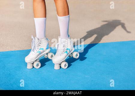Anonym von kurzen schwarzen weiblichen Beinen in weißen Socken und Quadroller-Sneakers, die auf blau-beigefarbenem Sportplatz stehen, mit Schatten an sonnigen Tagen Stockfoto