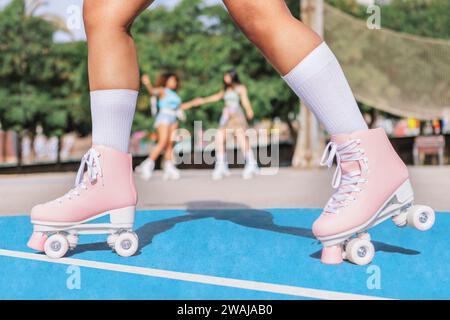 Seitenansicht der beschnittenen Beine einer anonymen jungen schwarzen Skaterin in weißen Socken und rosafarbenen Quad-Rollschuhen, die auf dem Sportplatz über Unschärfe reiten und skaten Stockfoto