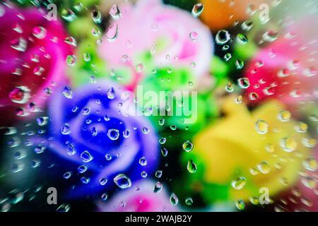 Wassertropfen auf Glas mit einem verschwommenen Hintergrund aus leuchtenden Blumen in Rosa-, Grün- und Blautönen Stockfoto