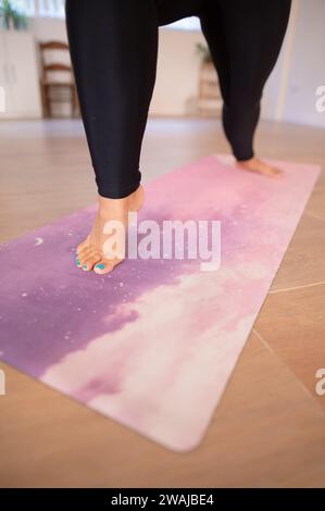 Barefoot-Frau in schwarzer Leggings, die während des Yoga-Fitnesstrainings auf einer lila Matte Dehnungsübung durchführt Stockfoto