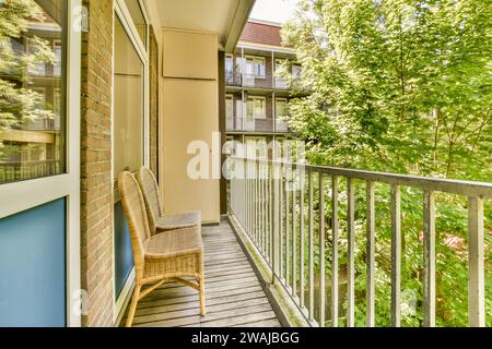 Leere korbstühle auf dem kleinen Balkon des modernen Apartments mit Fenstern und Ziegelwänden vor üppig grünen Bäumen Stockfoto