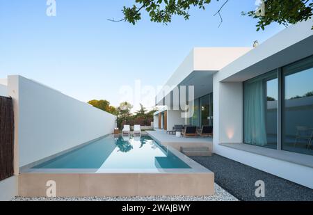 Modernes minimalistisches nachhaltiges Haus mit einem klaren blauen Pool mit eleganten weißen Wänden und einer ruhigen Himmelskulisse Stockfoto