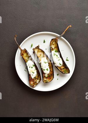 Gebackene Aubergine mit Knoblauch-Joghurt-Dressing auf Teller über dunklem Hintergrund mit freiem Platz. Draufsicht, flach Stockfoto