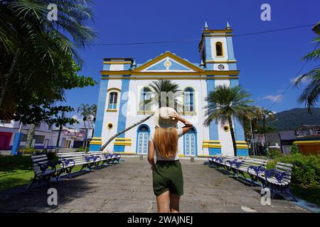 Tourismus in Brasilien. Rückansicht der jungen Touristenfrau vor der Kirche Igreja Matriz im historischen Zentrum von Ubatuba, Brasilien. Stockfoto
