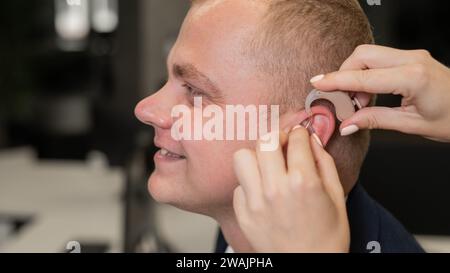 Frau, die ein Hörgerät auf einen kaukasischen Mann legt. Stockfoto