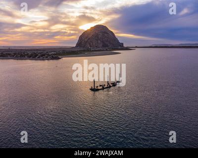 Morro Bay, Kalifornien, aus der Vogelperspektive auf den Morro Bay Rock und auf Seelöwen, die auf einem hölzernen Dock in der Mitte der Bucht liegen. Sonnenuntergang, bewölkter Himmel, Colorfu Stockfoto