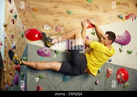 Muskulöser junger Mann, der künstliche Felsen an der Kletterwand klettert, Boulderaktivitäten in Innenräumen übt. Stockfoto