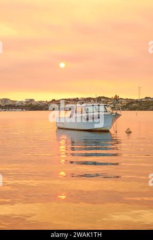 Ein Boot mit Reflexionen und gelbem und orangefarbenem Rauch, der von einem vorgeschriebenen Brand zur Verhinderung von Buschfeuer abgebrannt wird, Bicton, Swan River, Perth, Western Australia. Stockfoto