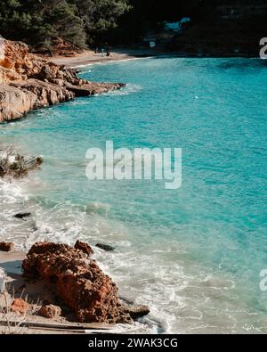 Ein malerischer Blick auf den Strand von Ibiza mit Fischerhütten, blauem Wasser und Felsen am Strand Cala Saladeta Stockfoto