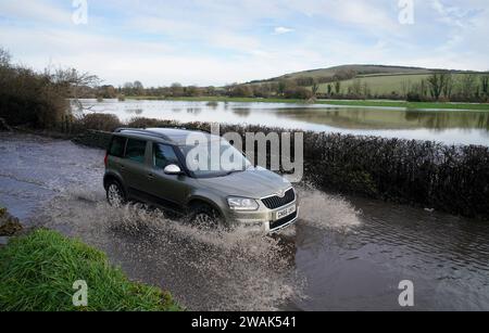 Ein Auto fährt durch das Hochwasser des Cuckmere River in Alfriston, East Sussex. Die Auswirkungen von Oberflächenwasser- und Flusspflutungen werden in Teilen Englands nach starken Regenfällen weiterhin „erheblich“ sein, warnten Experten. Bilddatum: Freitag, 5. Januar 2024. Stockfoto