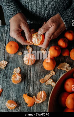 Hochwinkelansicht eines Mannes in einem grauen Pullover, der eine Mandarine auf einem grauen rustikalen Holztisch abblättert Stockfoto