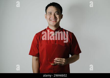 Glückliches Gesicht des asiatischen Mannes, der Cheongsam oder chinesisches traditionelles Tuch trägt, während er Angpao oder ein rotes Geldgeschenk auf weißem Hintergrund hält Stockfoto