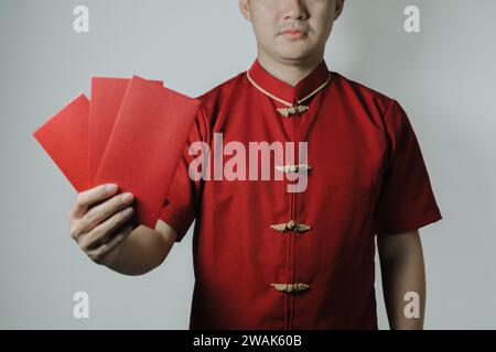 Asiatischer Mann mit Cheongsam oder chinesischem traditionellem Tuch hält Angpao und zeigt es der Kamera auf weißem Hintergrund. Gong Xi Fa Cai. Stockfoto