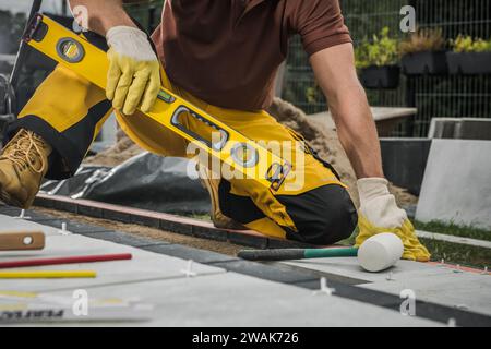 Bauarbeiter, der während der Installation von Betonziegeln eine Wasserwaage auf einer Terrasse überprüft Stockfoto